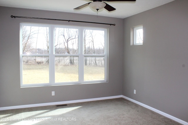 carpeted empty room featuring visible vents, a ceiling fan, and baseboards