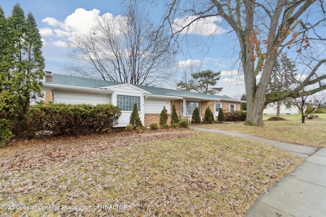 ranch-style house with a garage, brick siding, a chimney, and a front yard