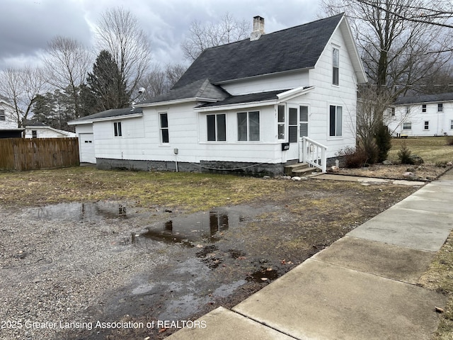 view of front of house with entry steps, a garage, a shingled roof, a chimney, and fence