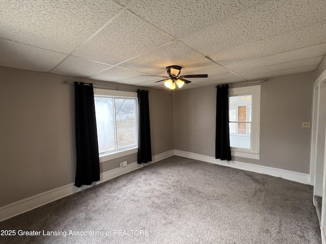 empty room featuring carpet floors, a ceiling fan, a paneled ceiling, and baseboards