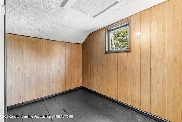 9840 W Herbison Rd, Eagle, MI 48822 - additional living space with dark wood-style flooring, wooden walls, and a textured ceiling
