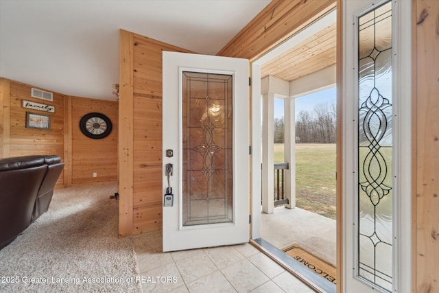 carpeted foyer entrance with tile patterned flooring, visible vents, and wooden walls