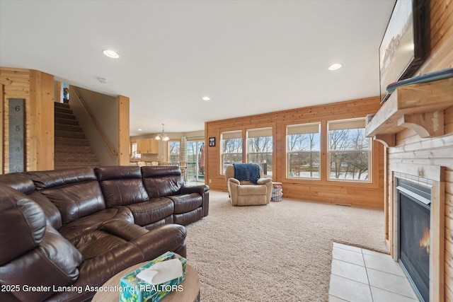 living area with light carpet, wood walls, a fireplace with flush hearth, and stairway