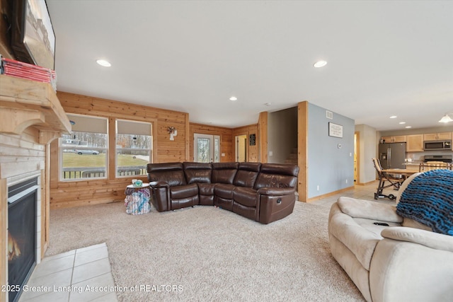 living area featuring a warm lit fireplace, light carpet, plenty of natural light, and wooden walls