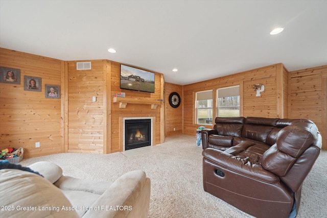 living room featuring carpet floors, a large fireplace, visible vents, and wooden walls