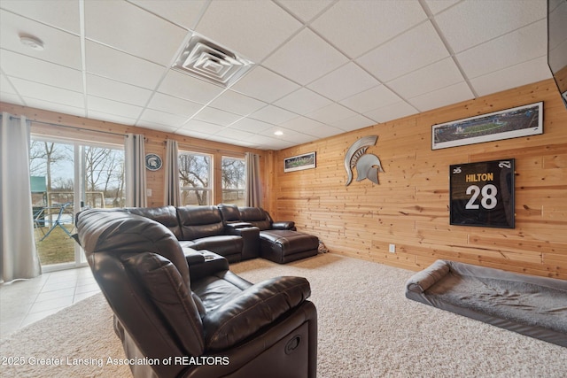 carpeted living room featuring wooden walls, a drop ceiling, and tile patterned floors