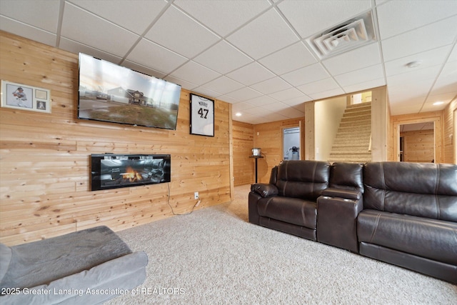 living room with carpet, visible vents, stairway, a glass covered fireplace, and wooden walls