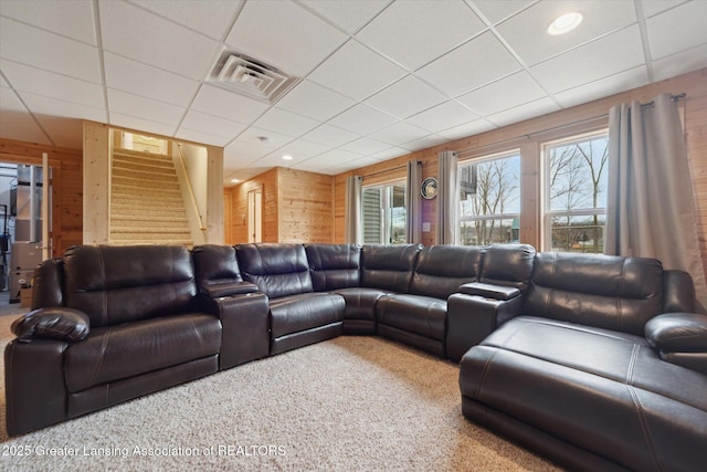 living room with wooden walls, visible vents, a drop ceiling, stairway, and carpet floors