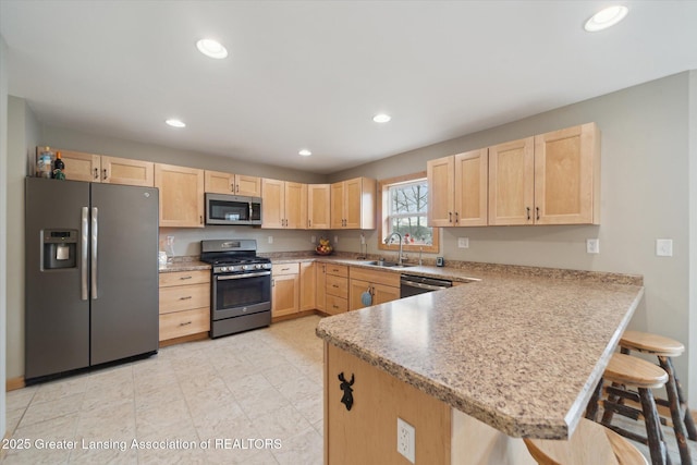 kitchen featuring appliances with stainless steel finishes, light brown cabinets, a sink, and a peninsula