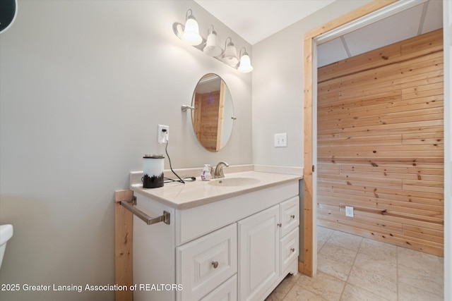 bathroom featuring toilet, vanity, and wooden walls