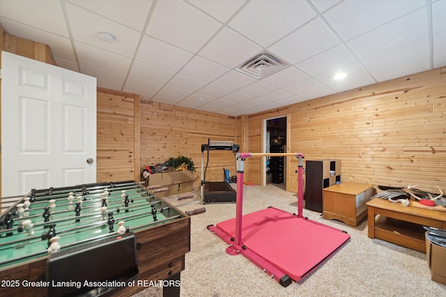 recreation room featuring carpet floors, a paneled ceiling, wood walls, and visible vents