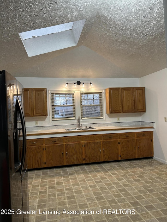 kitchen with brown cabinetry, light countertops, black refrigerator with ice dispenser, and a sink