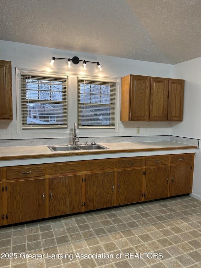 kitchen with tasteful backsplash, brown cabinetry, light countertops, a textured ceiling, and a sink