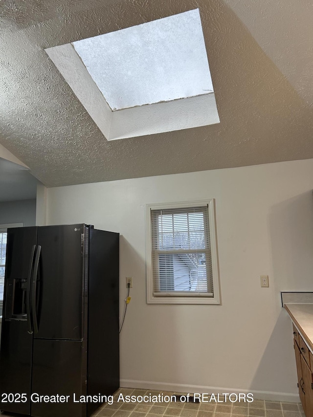 kitchen with a skylight, black fridge with ice dispenser, a textured ceiling, and baseboards