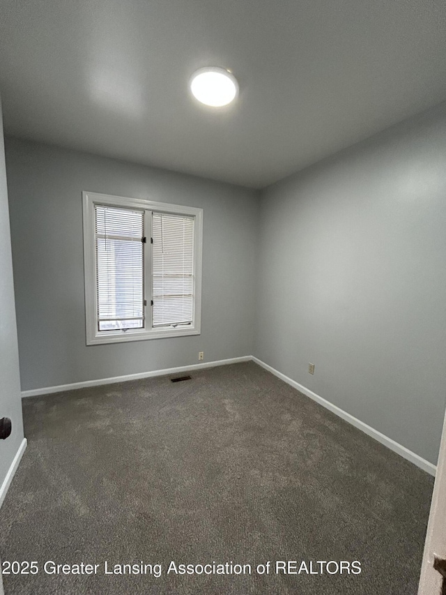 spare room with visible vents, dark carpet, and baseboards