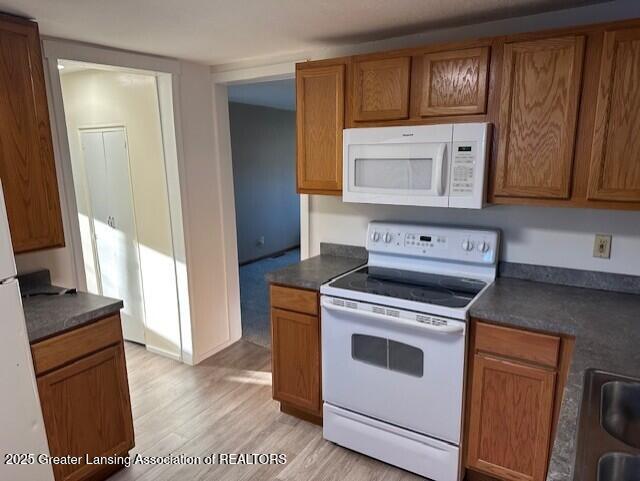 kitchen with dark countertops, white appliances, and light wood-style floors