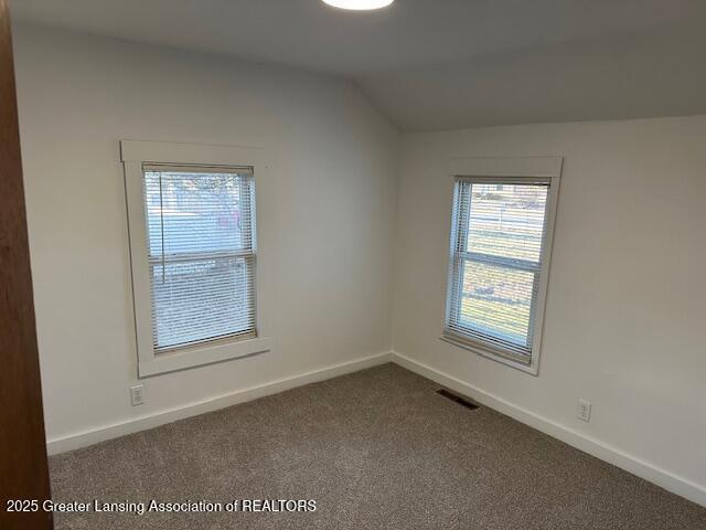 unfurnished room featuring lofted ceiling, baseboards, visible vents, and dark colored carpet