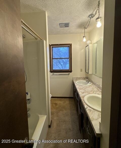 bathroom featuring a textured ceiling, double vanity, a sink, and visible vents