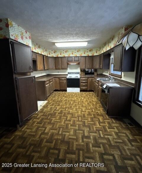 kitchen featuring white electric range oven, dark countertops, a textured ceiling, under cabinet range hood, and a sink