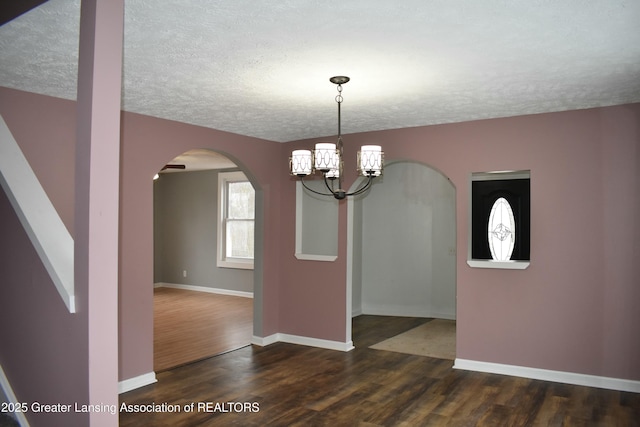 unfurnished dining area featuring arched walkways, a textured ceiling, baseboards, and wood finished floors