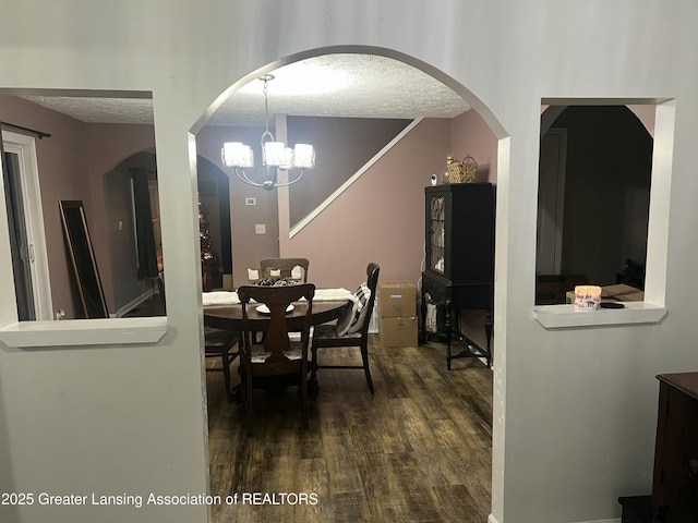 dining area with dark wood-style floors, a notable chandelier, arched walkways, and a textured ceiling