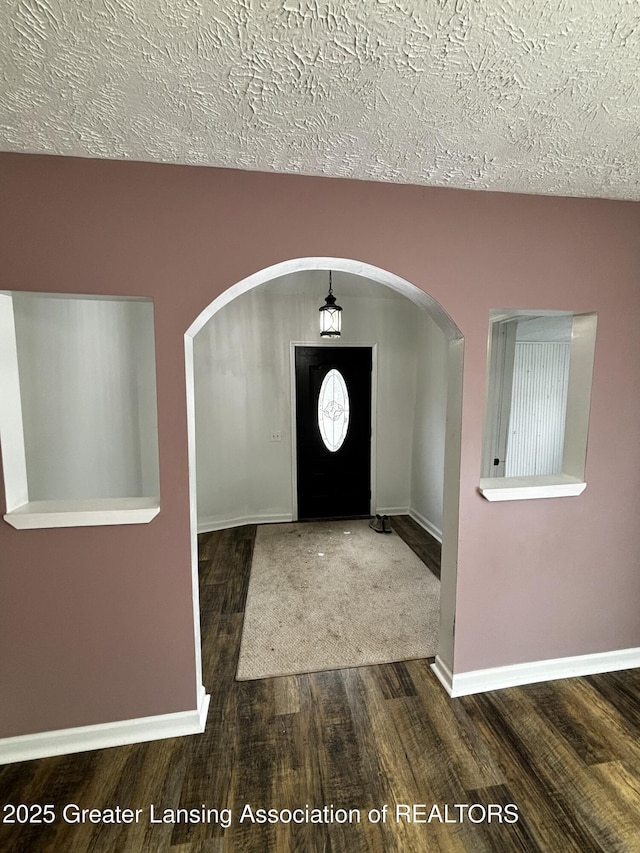 entrance foyer featuring baseboards, arched walkways, and wood finished floors