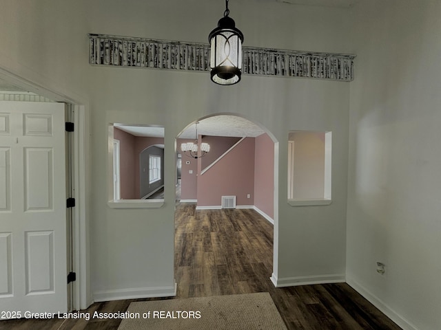 foyer entrance featuring arched walkways, dark wood finished floors, a notable chandelier, visible vents, and baseboards