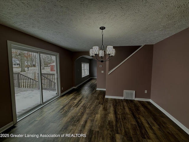 unfurnished dining area featuring an inviting chandelier, visible vents, baseboards, and wood finished floors