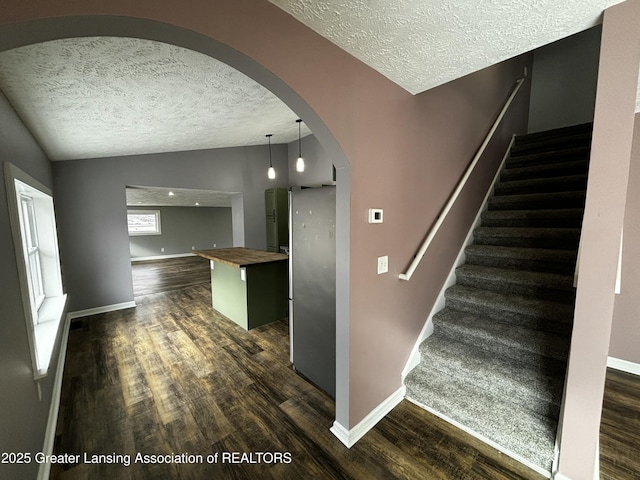 stairway featuring arched walkways, a textured ceiling, lofted ceiling, wood finished floors, and baseboards