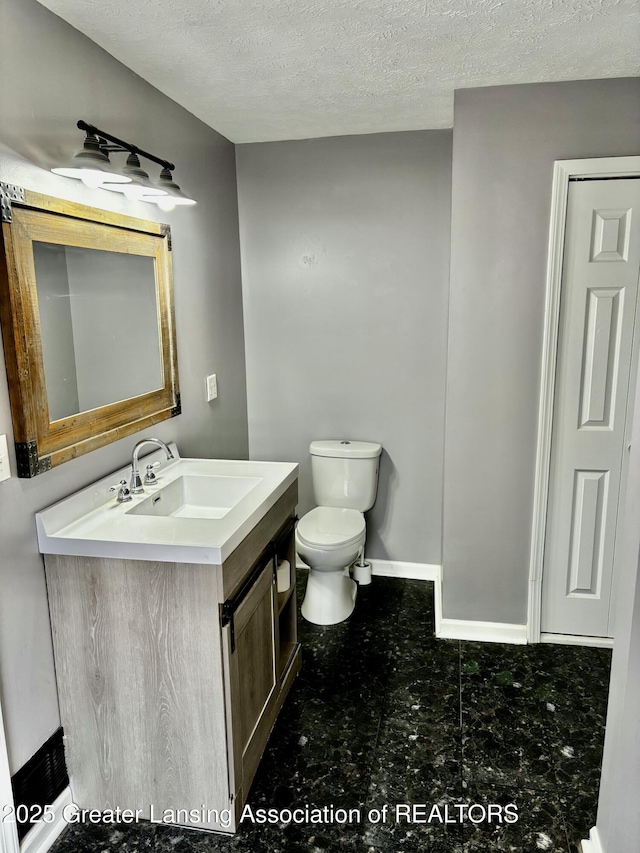 half bathroom with a textured ceiling, toilet, vanity, baseboards, and tile patterned floors