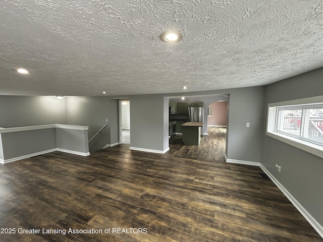 unfurnished living room featuring arched walkways, dark wood-type flooring, recessed lighting, and baseboards