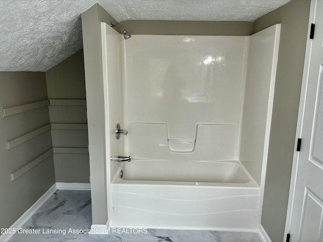 bathroom featuring a textured ceiling, marble finish floor, bathtub / shower combination, and baseboards