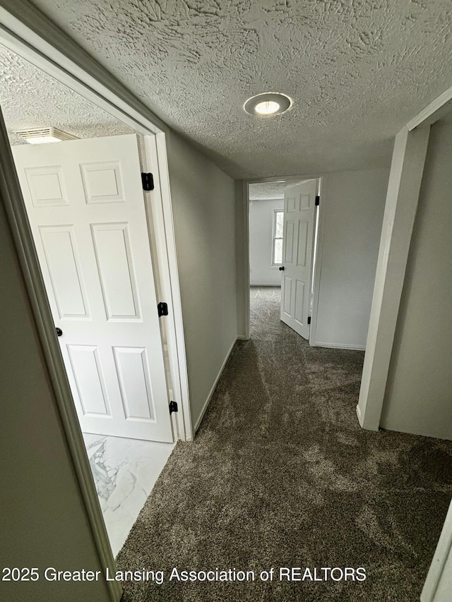 hall featuring a textured ceiling, baseboards, and carpet flooring