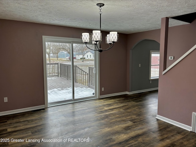 unfurnished dining area featuring dark wood-type flooring, arched walkways, plenty of natural light, and baseboards