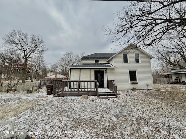 snow covered house with a shingled roof, fence, and a wooden deck