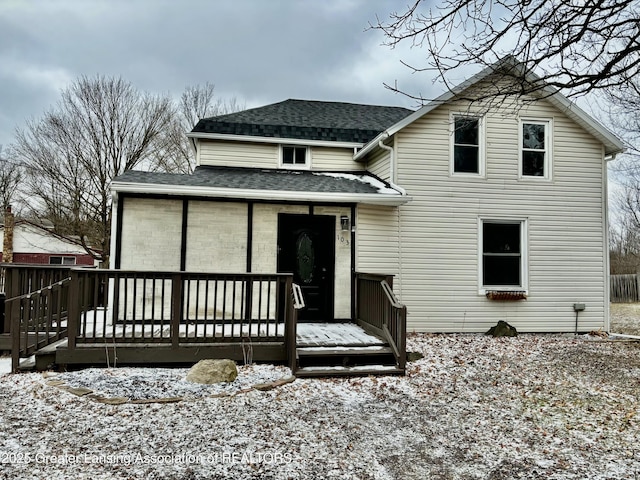 snow covered house with a shingled roof and a deck