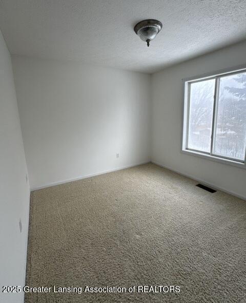 carpeted spare room featuring visible vents and a textured ceiling