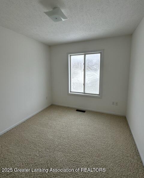 carpeted spare room featuring a textured ceiling and visible vents