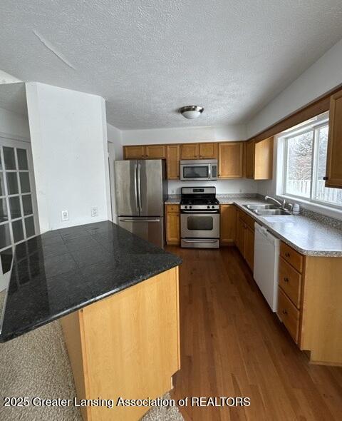 kitchen featuring dark wood-style flooring, appliances with stainless steel finishes, brown cabinetry, a sink, and a textured ceiling