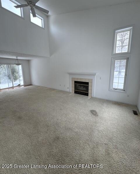 unfurnished living room with a tile fireplace, a high ceiling, visible vents, a ceiling fan, and carpet