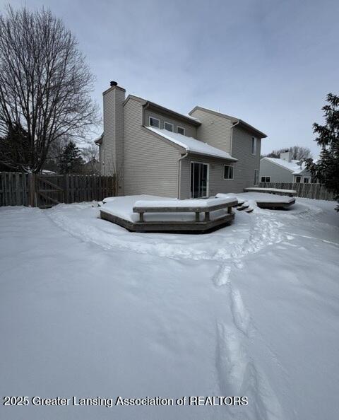 snow covered house with a chimney and fence