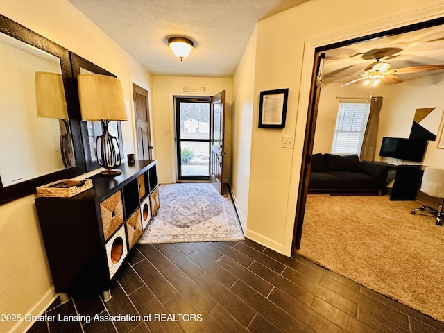 doorway featuring dark wood-style floors, ceiling fan, baseboards, and a textured ceiling