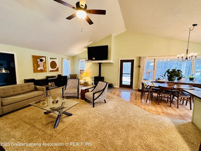 living area with ceiling fan with notable chandelier, high vaulted ceiling, wood finished floors, and baseboards