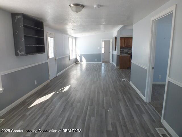 unfurnished living room featuring dark wood-style floors, visible vents, and baseboards