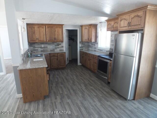 kitchen with appliances with stainless steel finishes, backsplash, a sink, and brown cabinets