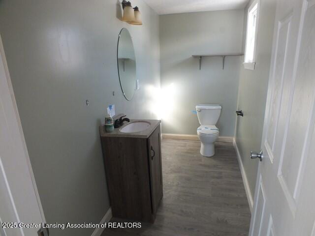 half bathroom featuring vanity, wood finished floors, toilet, and baseboards