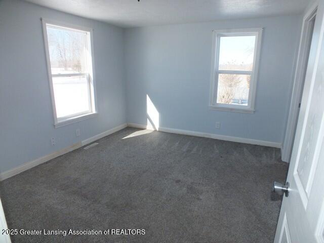 empty room with baseboards, visible vents, and dark colored carpet