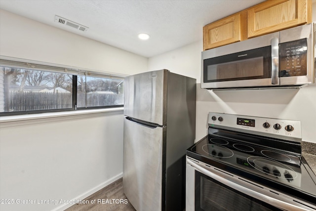 kitchen with light brown cabinets, wood finished floors, visible vents, baseboards, and appliances with stainless steel finishes