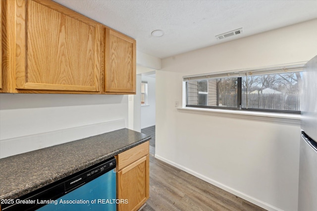 kitchen featuring dishwashing machine, wood finished floors, visible vents, baseboards, and dark countertops