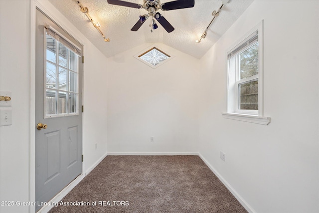 carpeted empty room with a textured ceiling, a ceiling fan, baseboards, vaulted ceiling, and rail lighting